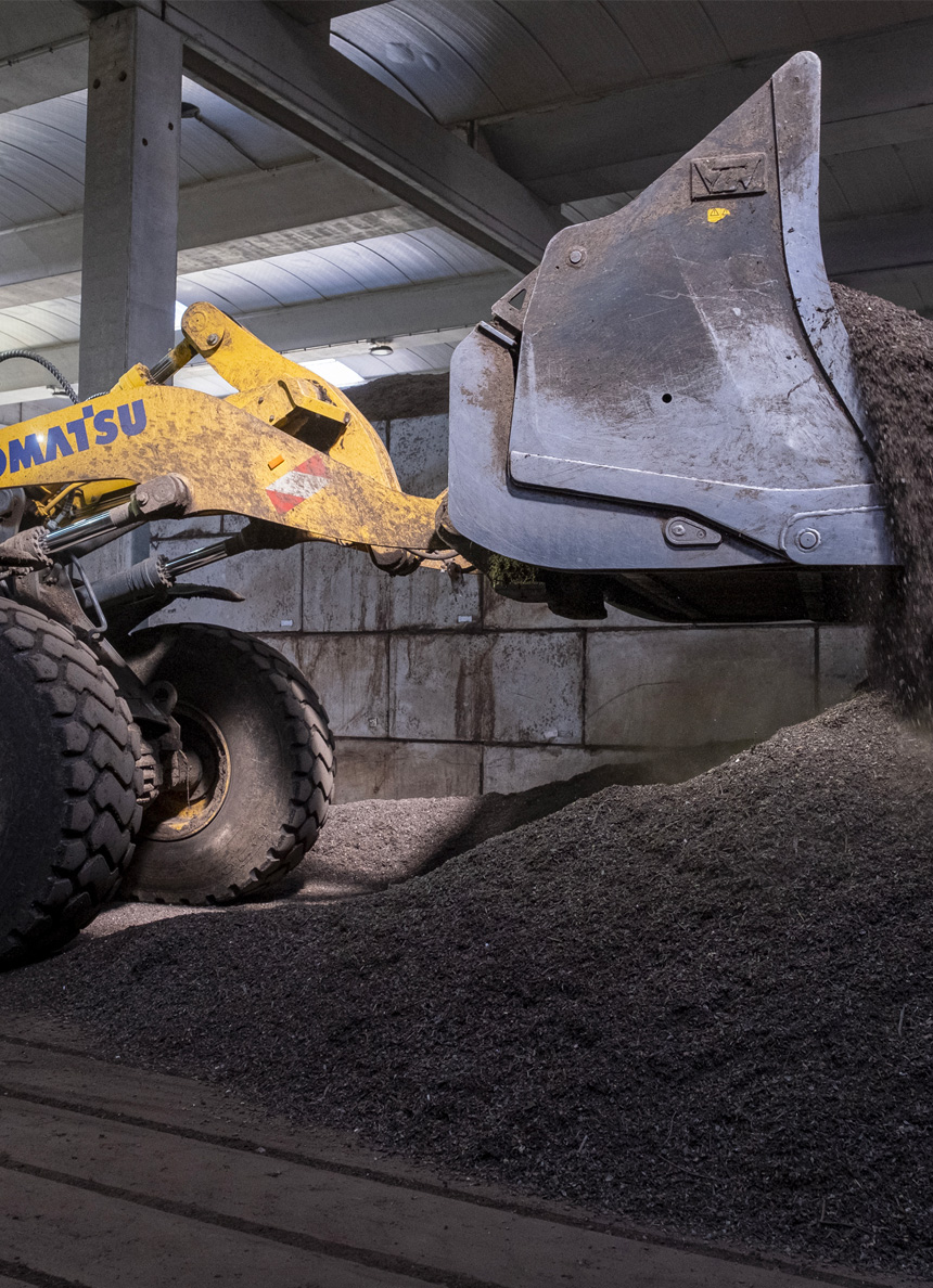 Un caricatore frontale giallo Komatsu di Acea Ambiente sta scaricando un carico di materiale sfuso scuro, formando un cumulo a terra