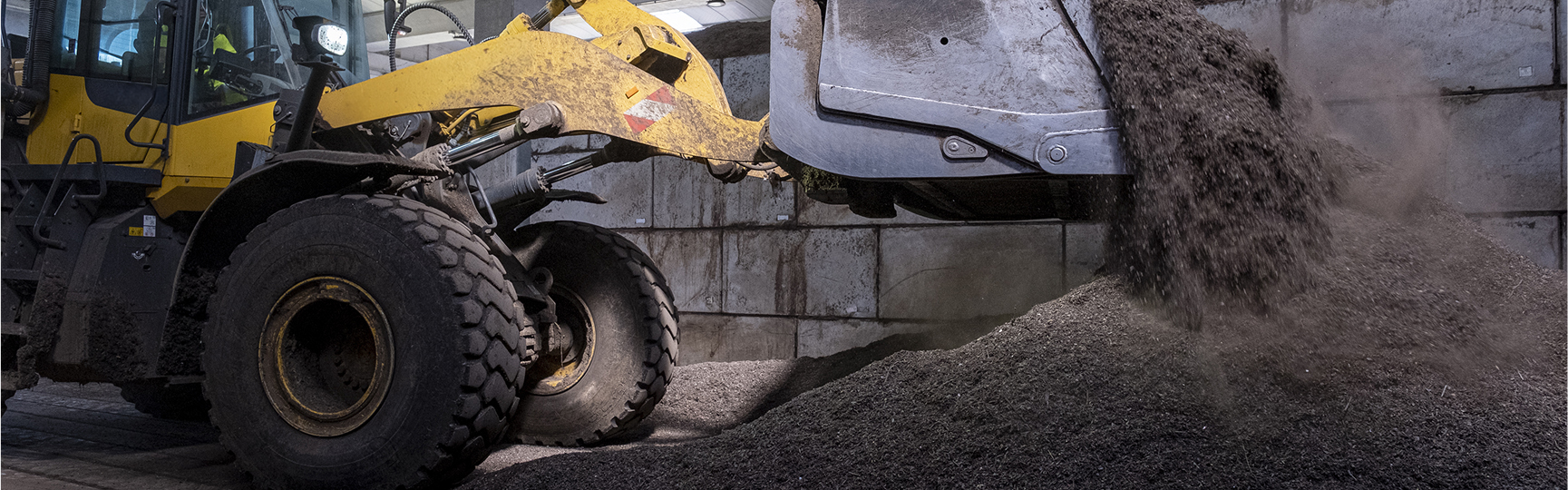 Un caricatore frontale giallo Komatsu di Acea Ambiente sta scaricando un carico di materiale sfuso scuro, formando un cumulo a terra