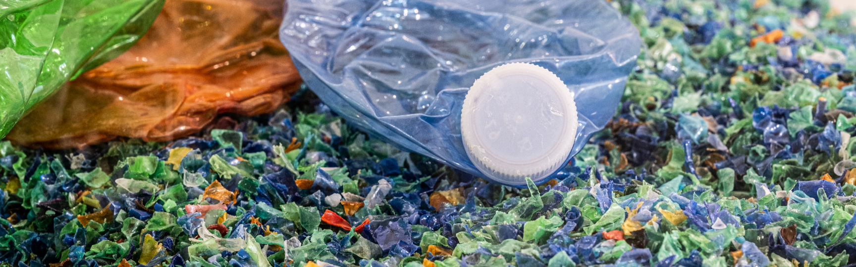Bottiglie di plastica schiacciate su un letto di frammenti colorati di plastica riciclata